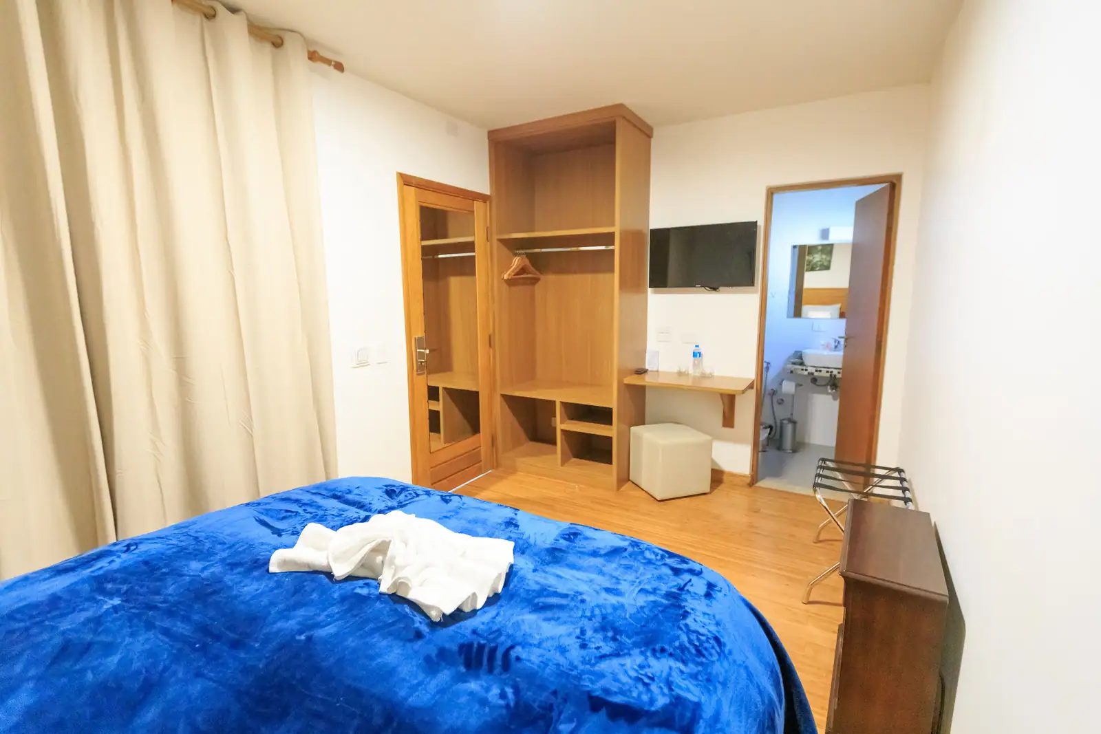 Chambre d'hôtel compacte : lit, penderie ouverte, écran mural et porte de la salle d'eau restée ouverte