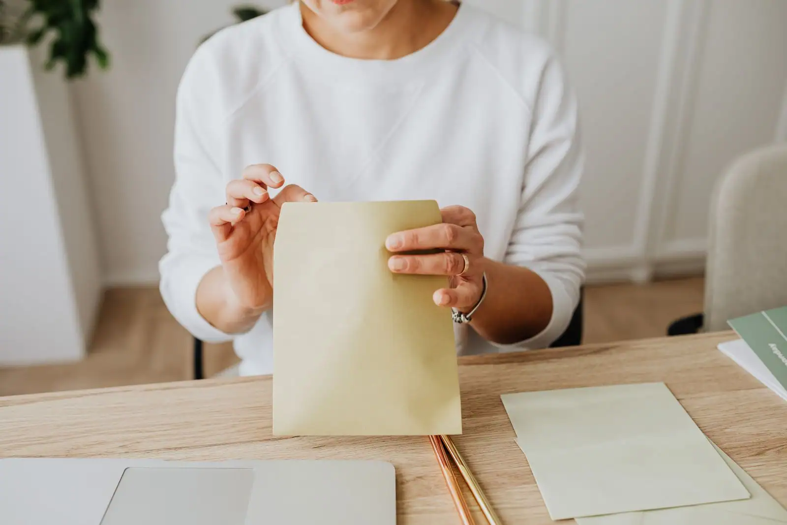 Mains refermant une enveloppe kraft sur une table en bois clair, à côté de deux feuilles de papier.