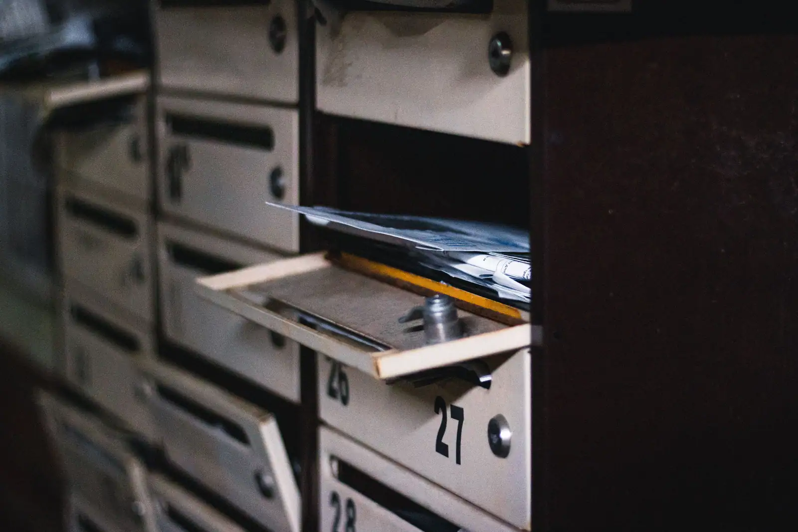Boîte aux lettres d'immeuble entrouverte, courrier glissé à l'intérieur, numéros peints sur les portes voisines.