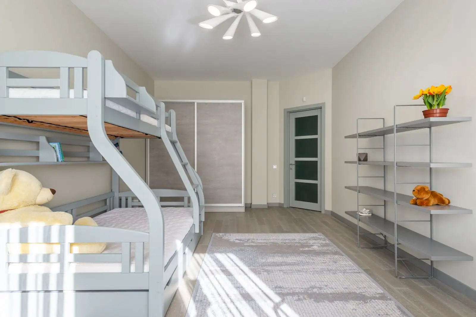 Une chambre d'enfants avec un lit superposé gris, un couchage large en bas et un couchage simple en haut.