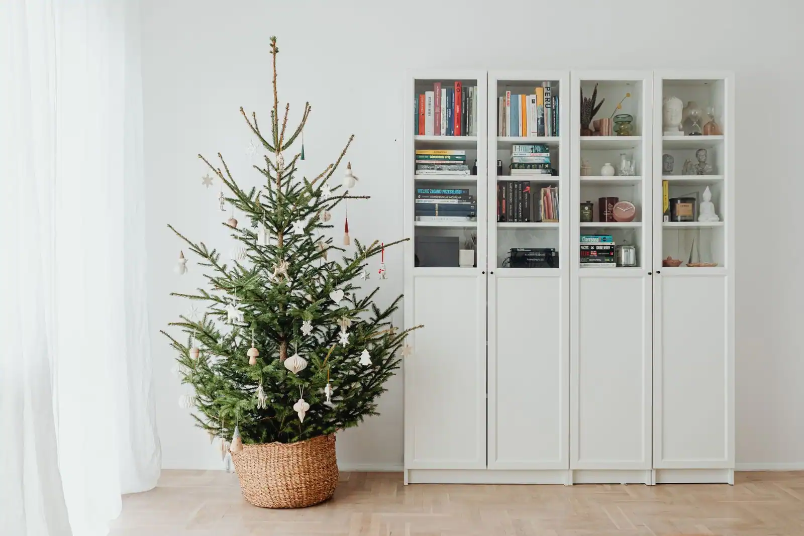 Sapin naturel sobrement décoré dans un panier, posé près d'une bibliothèque blanche dans un séjour.