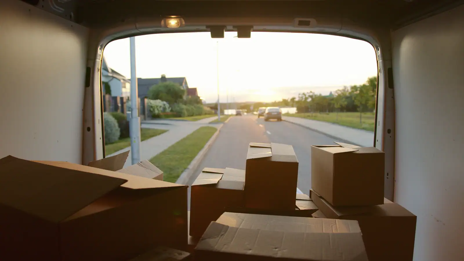 Vue depuis l’intérieur d’un fourgon chargé de cartons, portes arrière ouvertes sur une route de lotissement.