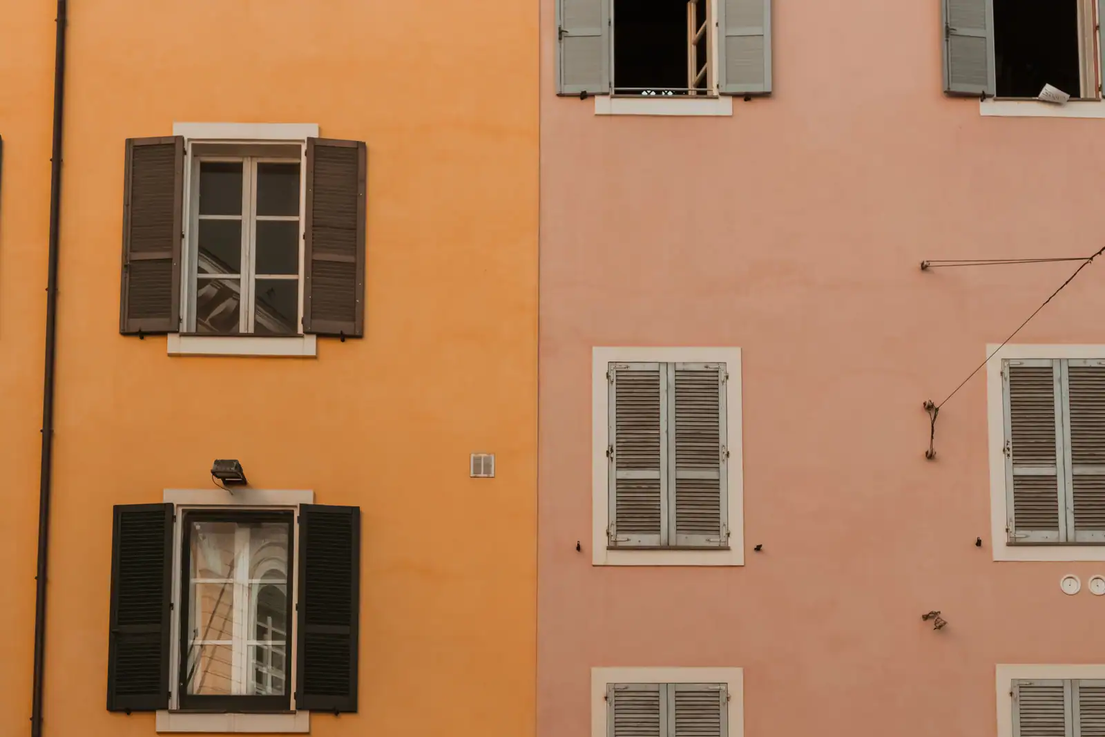 Deux façades d'immeubles d'habitation mitoyennes, l'une ocre l'autre rose, aux fenêtres à volets battants.