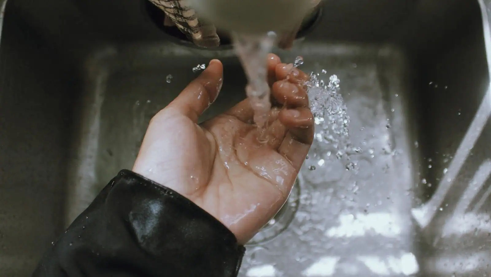 Main ouverte, paume vers le haut, tenue sous un filet d'eau courante dans un évier en inox