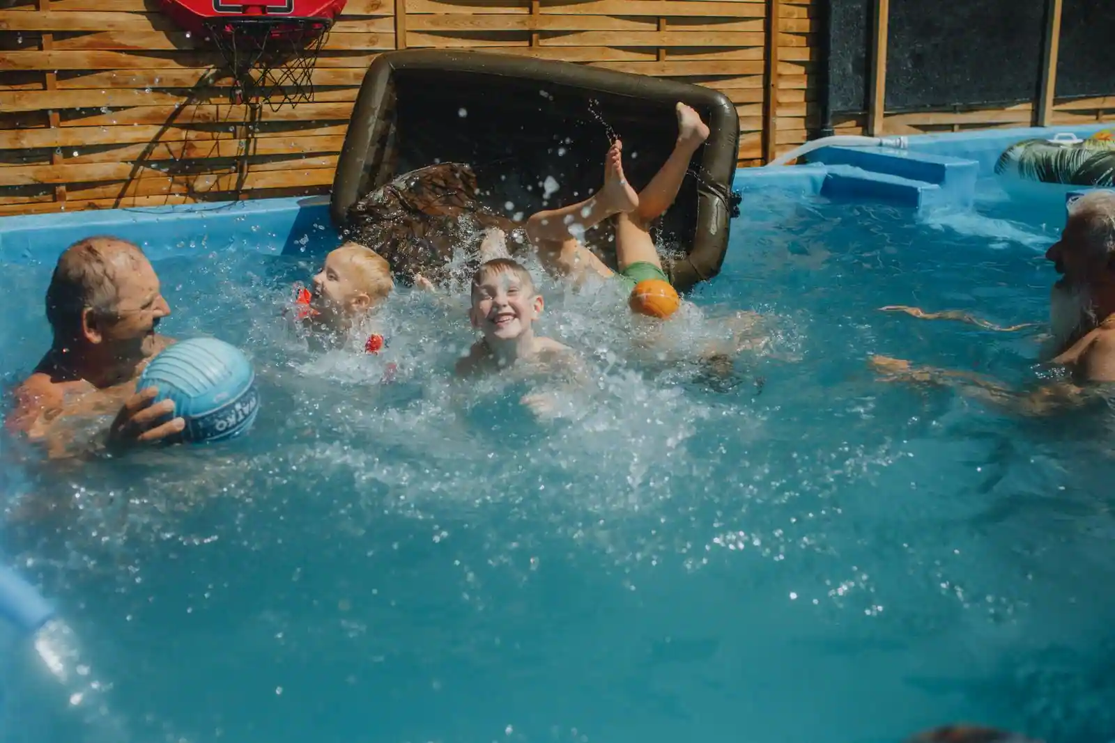 Adulte et enfants dans une piscine hors sol à paroi souple, installée dans un jardin clos de brise-vue