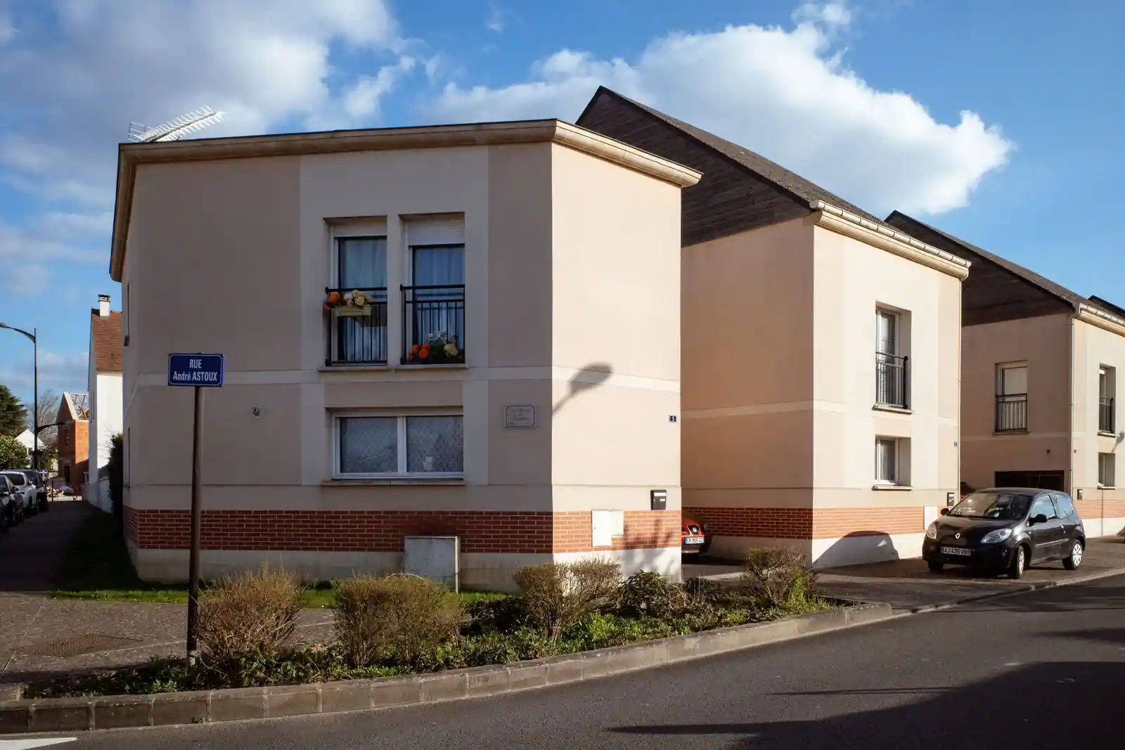 Maisons mitoyennes à façades enduites beige et soubassement de brique, à l'angle d'une rue de Compiègne.