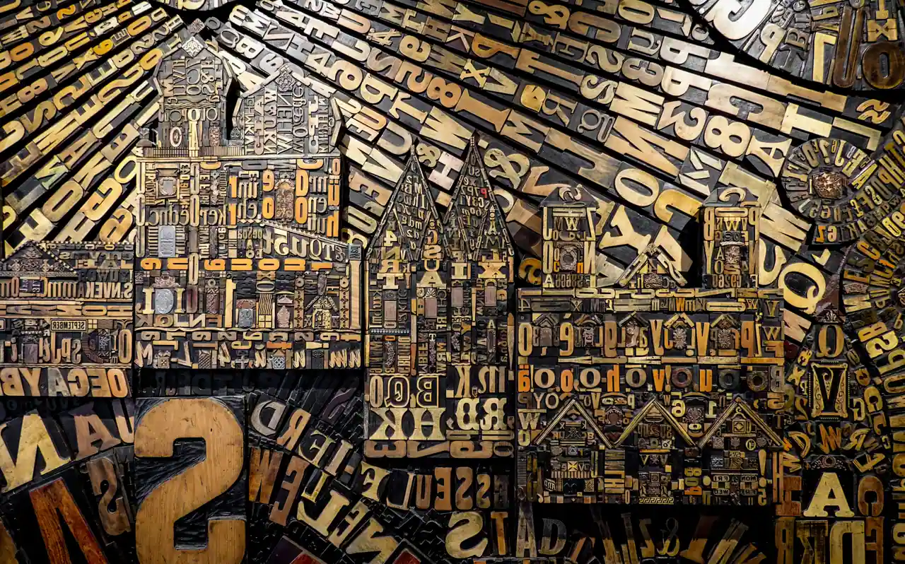 Assemblage mural de caractères d’imprimerie en bois composant des façades de maisons et un clocher.