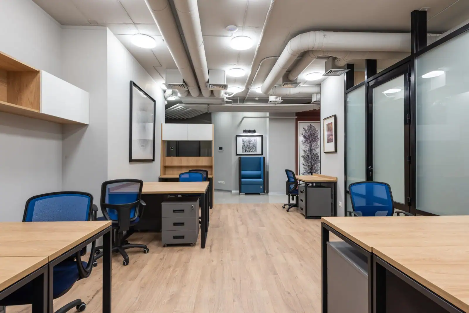 Plateau de bureaux meublé mais inoccupé, postes en bois clair, cloisons vitrées et gaines apparentes